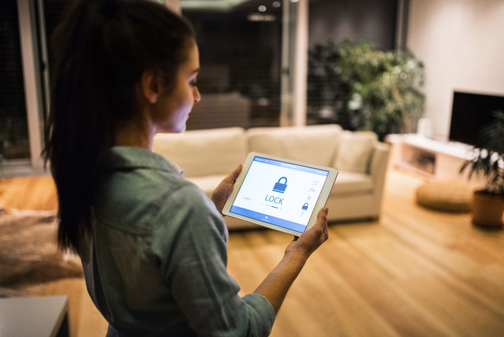 A woman standing in her living room using a tablet to control her home security system